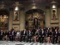 Una reunión formal en una iglesia con un altar dorado, personas sentadas y otros de pie.
