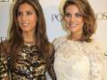 Dos mujeres con vestidos elegantes posan frente a un fondo de publicidad.