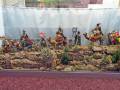 Un diorama con figuras de soldados y camellos en una escena histórica, rodeado por vegetación artificial.