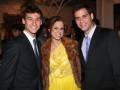 Tres personas sonrientes en un evento formal, dos hombres con trajes y una mujer con abrigo de piel.