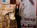 A una mujer con un bolso blanco y una chaqueta beige, posando frente a un cartel de la Feria Internacional del Caballo Sicab 2012. La feria se celebra del 20 al 25 de noviembre en la Plaza de Convencciones y Exposiciones de Málaga.