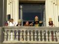 Un grupo de personas disfrazadas en trajes tradicionales, posiblemente para un evento festivo o celebración. La imagen muestra a las personas en una balconada de un edificio, con algunos sujetando copas y otros mirando hacia abajo. La decoración del edificio y los trajes sugieren una celebración o festividad especial.
