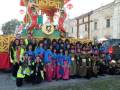Una gran carpa de color amarillo y rojo con figuras de dioses chinos, una batería grande y un grupo de personas vestidas con trajes tradicionales posando para una foto.