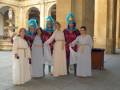 Grupo de personas vestidas con trajes tradicionales posando frente a una arquitectura histórica.