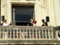 Músicos tocando en un balcón histórico con espectadores en la plaza.