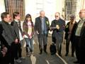 Una reunión de negocios en una calle de la ciudad, con personas vestidas formalmente y una persona con una mochila negra en el suelo. El ambiente sugiere un evento profesional.
