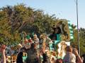 Desfile de carnaval con disfraces coloridos y figuras gigantes en el cielo azul.