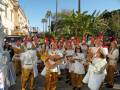 Desfile festivo con músicos y bailarines en trajes tradicionales.