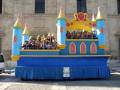Un carnaval de Disneyland Paris con un carro temático azul y amarillo, adornado con detalles dorados y decoraciones rojas. Los participantes son niños vestidos de disfraces, con sombrillas y sombreros, en una plataforma elevada. La imagen muestra un ambiente festivo y colorido típico de Disneyland Paris.