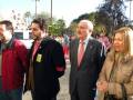 Un grupo de personas caminando en una calle con árboles y un parque en el fondo.
