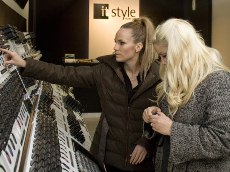 Dos mujeres en una tienda de moda, una selecciona un accesorio mientras la otra observa.
