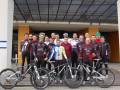 Equipo ciclista posando con bicicletas frente a un edificio moderno.