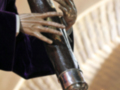 Una mano sosteniendo un candelabro de metal en una iglesia. La mano está vestida con guantes y sostiene la vela encendida en el candelabro. La iluminación es suave, con una luz que se proyecta desde el candelabro hacia la vela. La atmósfera es tranquila y reverente, típica de un ambiente religioso.