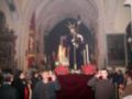 Procesión religiosa en una iglesia con imágenes de santos y personas participantes rezando.