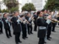 Músicos militares tocan instrumentos en una banda militar, con árboles y edificios al fondo.