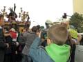 Una procesión religiosa con una imagen de Cristo en el centro, rodeada por fieles y fotógrafos. La gente está observando atentamente la imagen mientras otros se preparan para tomar fotos. El cielo es claro y el ambiente parece ser de un día soleado.
