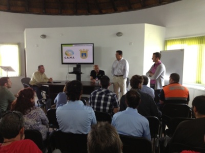 Presentación en sala de conferencias con un hombre hablando frente a una pantalla con el logo de C.A.N.S.