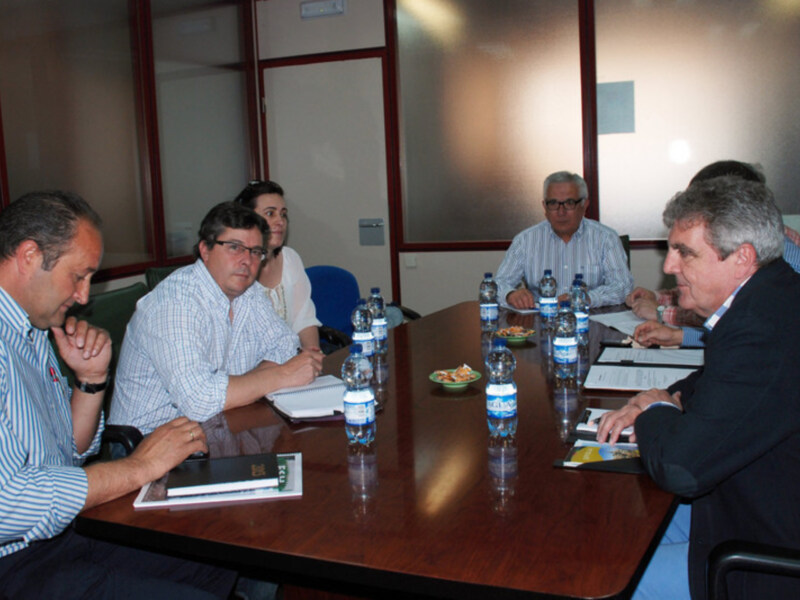 Un grupo de personas reunidas en una sala de conferencias, sentadas en mesas y trabajando en documentos. Hay botellas de agua en la mesa y una persona con una camisa blanca y un hombre con una camisa azul son los principales sujetos de la imagen.