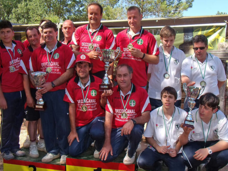 Equipo ganador con trofeos y medallas celebrando su victoria en un evento deportivo al aire libre.