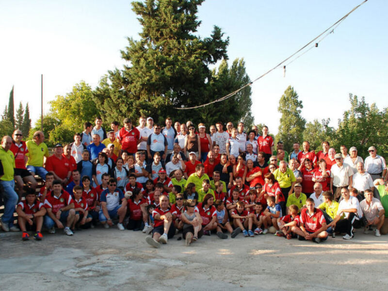Una gran reunión de personas en un parque, todos sonrientes y vestidos con camisetas de equipos deportivos, posiblemente en un evento de fútbol o similar.