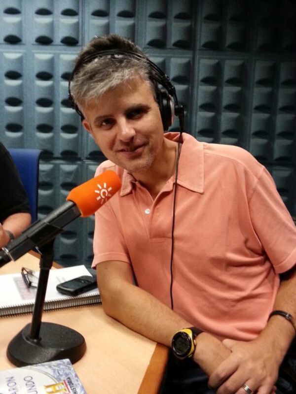 Un hombre con auriculares y una camisa rosa está en una radio, posando para una foto.