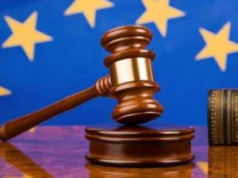 Un martillo de juez sobre un libro, con el fondo de la bandera de la Unión Europea, simbolizando la aplicación de la justicia europea en el ámbito legal europeo.