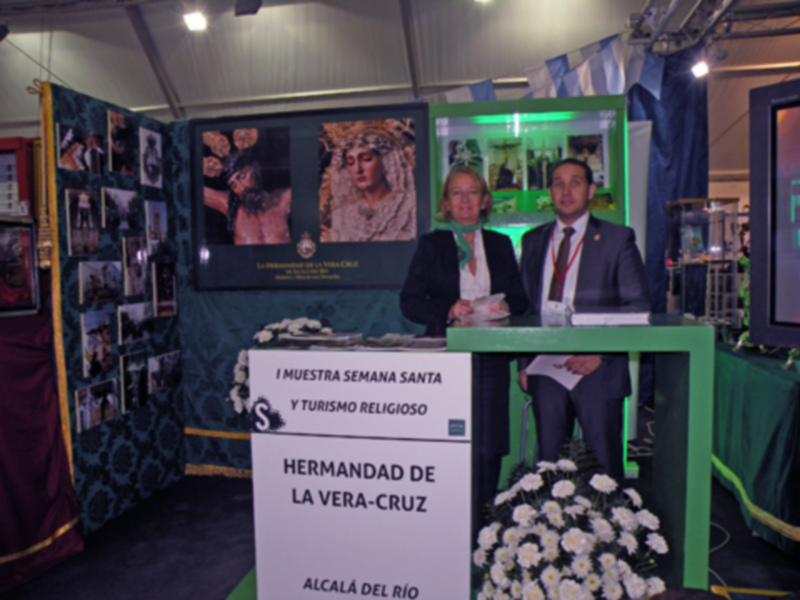 Exposición de Semana Santa en Alcalá de Río, con stands informativos y flores blancas.