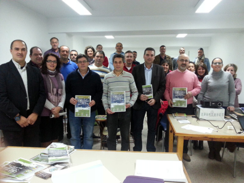 Un grupo de personas posando para una foto en una sala de conferencias, sosteniendo folletos y sonriendo.