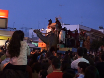 Desfile nocturno con carroza y personajes vestidos de trajes tradicionales en una ciudad.