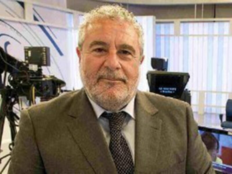 Un hombre con barba y bigote, vestido de traje, frente a una cámara de televisión.