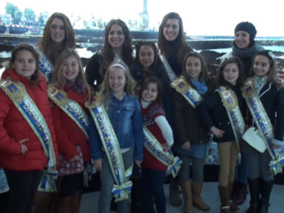 Grupo de niñas con coroas y sashes posando en una pista de patinaje.