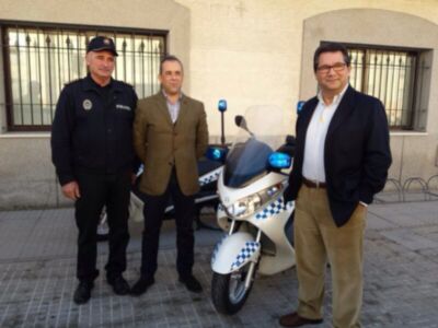 Tres hombres posan frente a una motocicleta policía, con un edificio de fondo y ventanas.