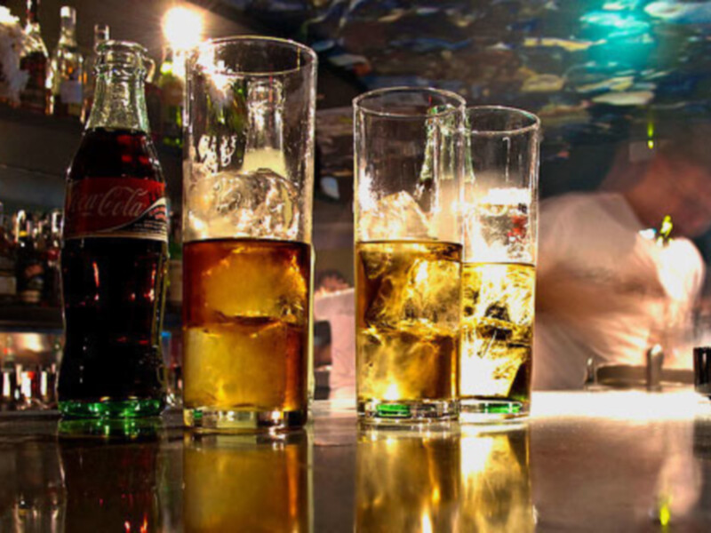 Tres vasos de cerveza y una botella de Coca-Cola en un bar con luces brillantes.