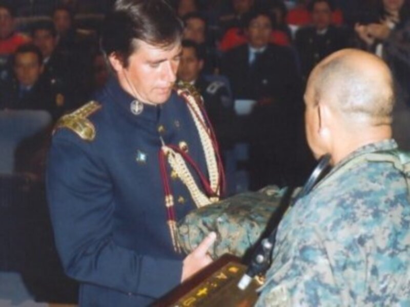 Un hombre en uniforme militar entrega un reconocimiento a un soldado en un auditorio lleno de personas.