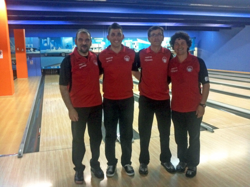 Cuatro personas en uniforme rojo posan frente a una pista de bowling.