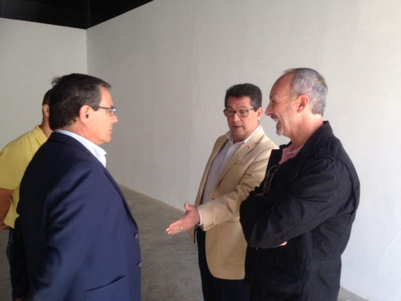 Tres hombres conversando en un entorno interior, uno de ellos estrechando la mano del otro.