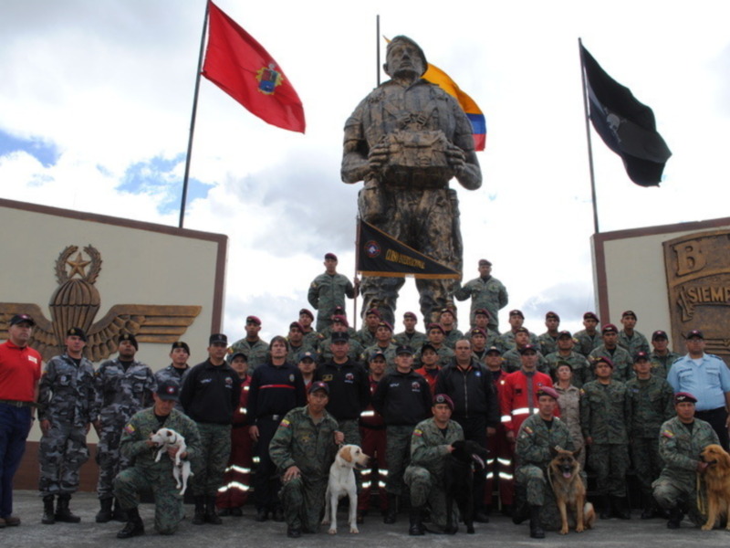 Un grupo de soldados posa frente a una estatua y banderas, con un perro en el centro de la imagen.