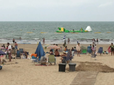 Playa con gente relajándose, sombrillas, sillas y un parque acuático en el agua.