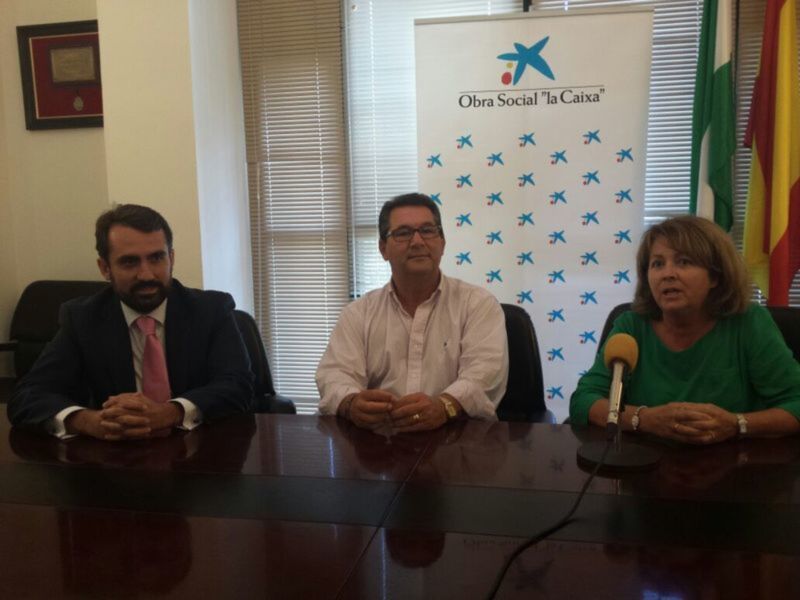 Tres personas sentadas en una sala de conferencias, con un fondo que muestra la bandera de la Caixa y una persona con un micrófono en la mesa.