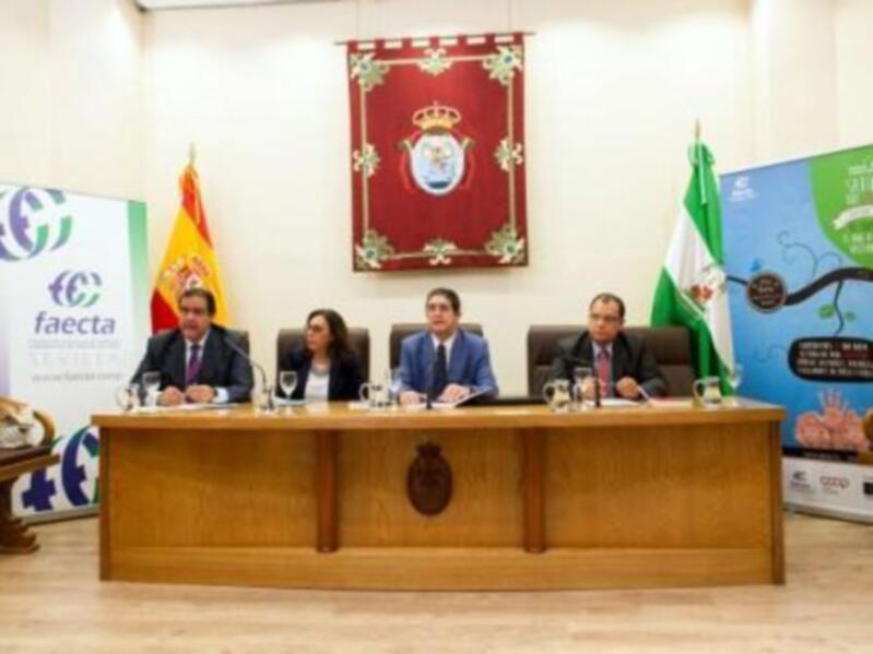 Presentación oficial en un salón de conferencias con cuatro personas sentadas en una mesa. En el fondo, banderas y un escudo heráldico destacan la importancia del evento.