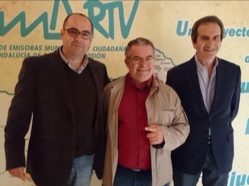 Tres personas posando frente a un fondo con la inscripción 'EMTV' y un mapa de Andalucía.