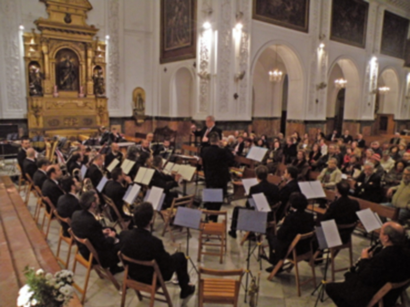 Orquesta sinfónica en un concierto en una sala de conciertos histórica, con músicos en el escenario y público sentado en el auditorio.