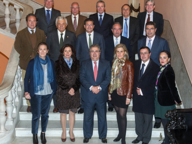 Una imagen de una reunión formal en un entorno elegante, con una escalera y paredes de color claro. La escena incluye a varias personas vestidas con trajes formales y chaquetas, posando en una fila. La imagen transmite un ambiente de respeto y profesionalismo.