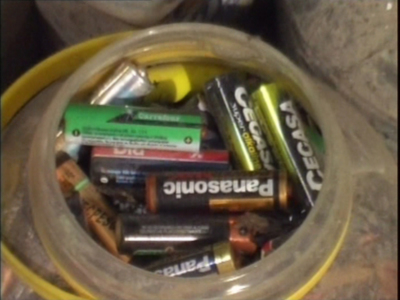 Un recipiente lleno de pilas de diferentes marcas y tamaños, incluyendo CECASA, Panasonic y Duracell, en un entorno de almacenamiento de pilas.