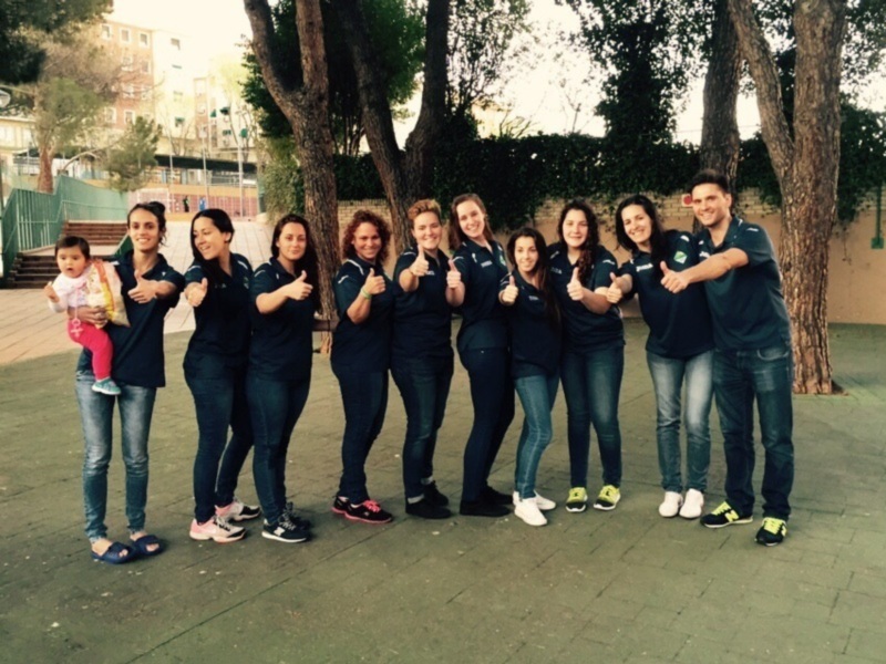 Una familia feliz posando juntos en un parque. La mamá sostiene a su bebé, mientras los demás miembros de la familia dan un gesto de apoyo con sus manos. Todos están vestidos con ropa casual, y el entorno es tranquilo con árboles y una valla en el fondo.
