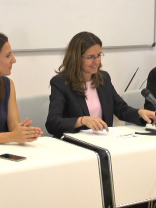Tres mujeres sentadas en una mesa de conferencia, con un tablero blanco y un teléfono móvil a su lado.