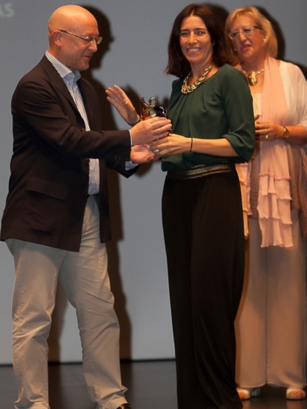 Una persona recibe un premio mientras sonríe y sonríe, mientras otra persona observa en segundo plano.