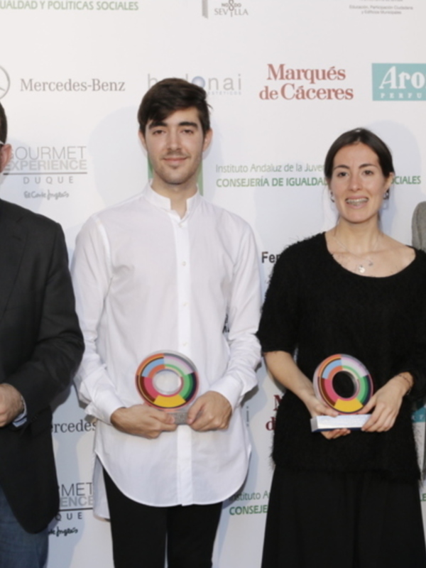 Ganadores de un premio en una ceremonia de reconocimiento, con un fondo blanco y logos de patrocinadores en el fondo.
