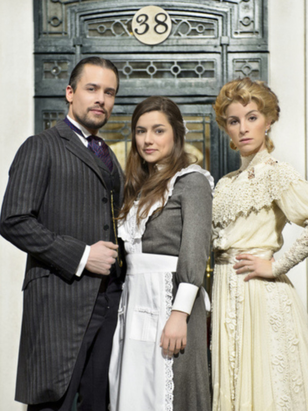 Tres personas posan frente a una puerta de madera con el número 38. La imagen sugiere un ambiente histórico o elegante, posiblemente en el siglo XIX.