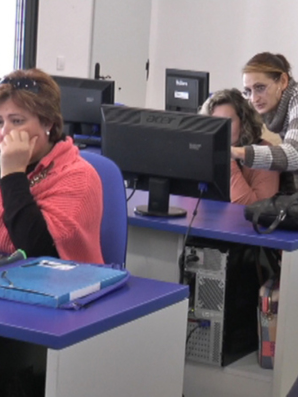 En una clase de informática, estudiantes están sentados frente a sus computadoras, concentrados en sus tareas. La imagen muestra una escena de aprendizaje y estudio en un entorno educativo moderno.